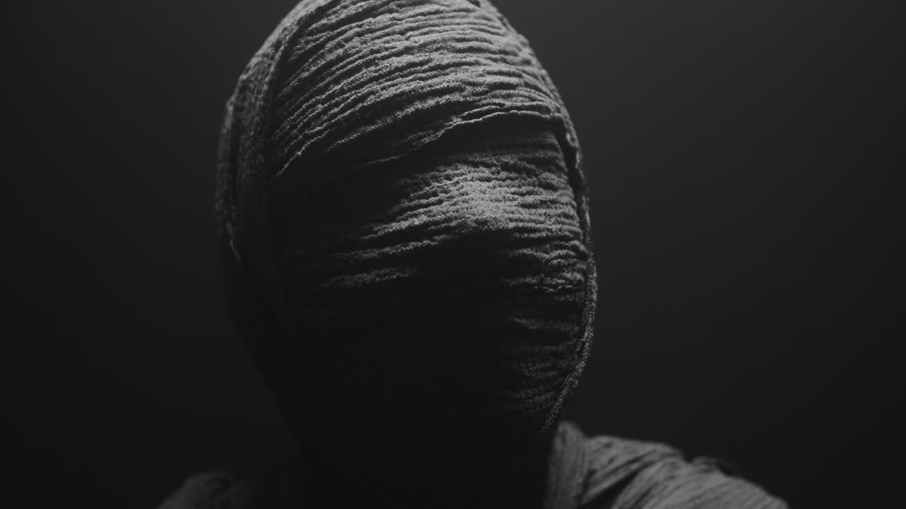 A mummy of a woman on a dark backdrop slowly rises her head
