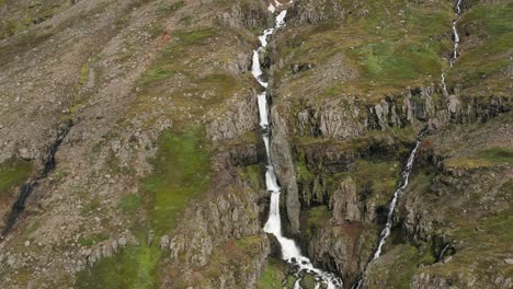 Melt-water-waterfall-on-rocky-slope-of-remote-Iceland-mountain,-aerial