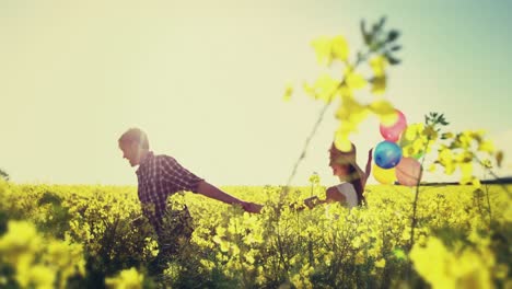 romantic couple holding colorful balloons and running in mustard field