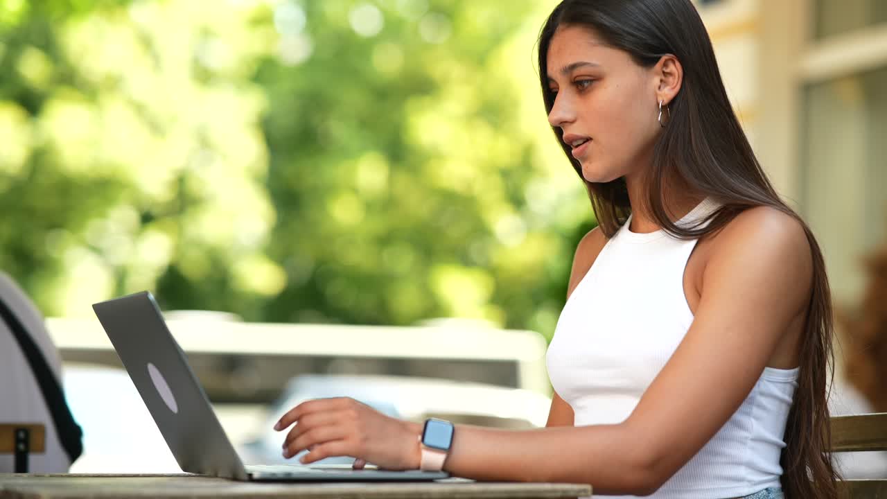 mujer joven trabajando en una computadora portátil en un café al aire libre