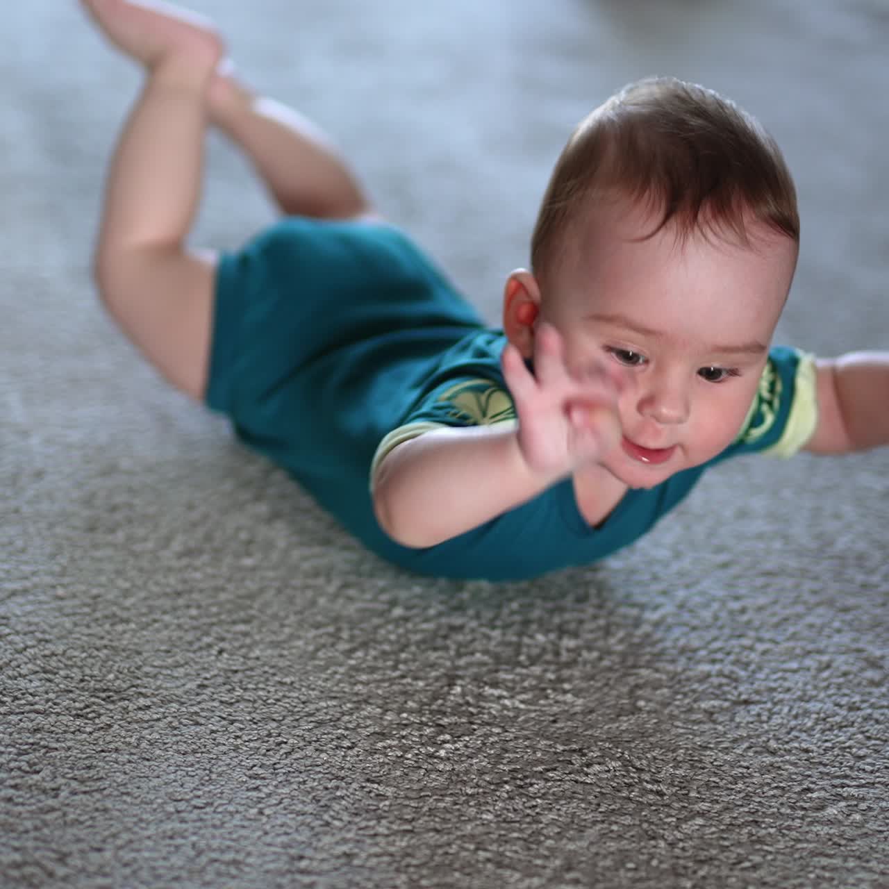 Nice baby boy lies on the floor looking up to the camera with surprise. Funny little child banging arms and legs by the floor