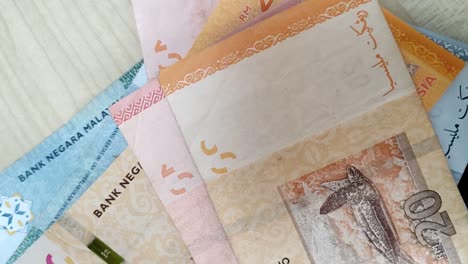 several malaysian banknotes of various denominations are placed one by one on a beige-colored table, showcasing the currency's distinct features and intricate designs.