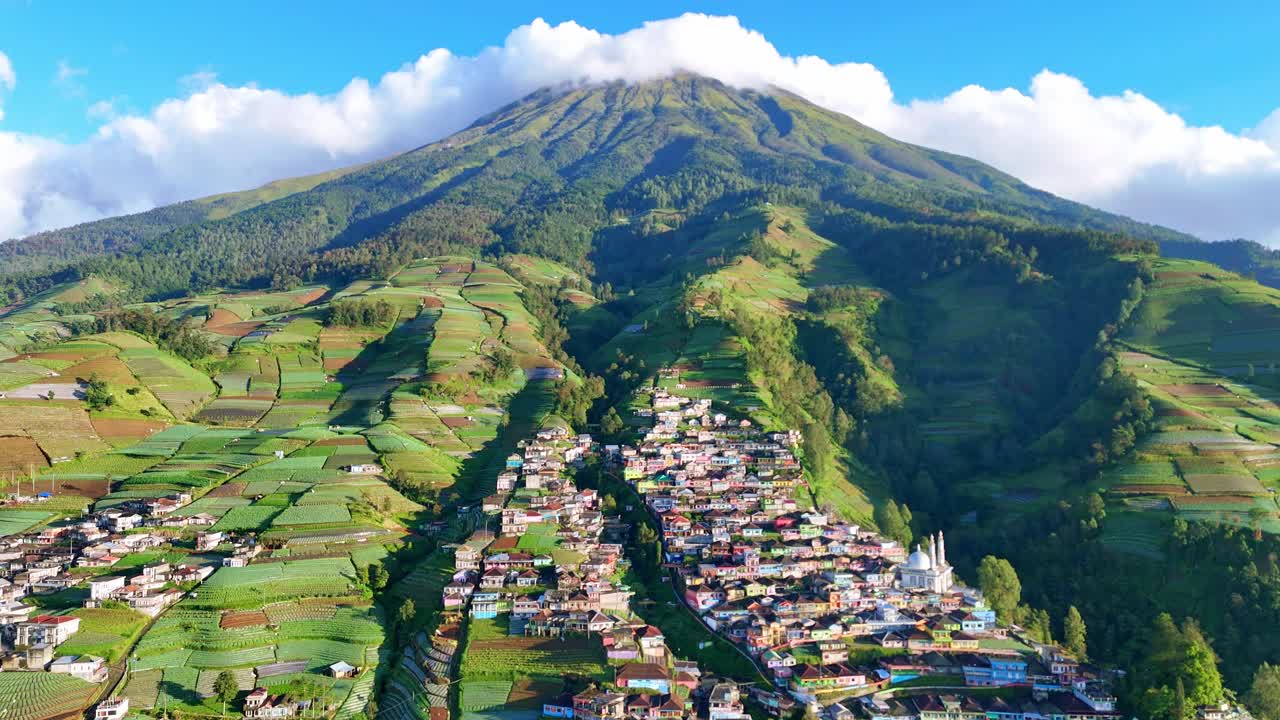Panoramic aerial video showing a densely packed mountain village surrounded by terraced farmland and natural greenery. Nepal Van Java Village, Mount Sumbing, Indonesia