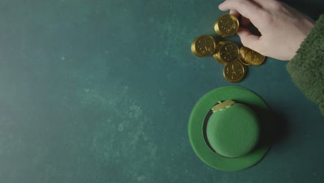 foto de estudio superior de sombrero de copa de duende verde y mano recogiendo monedas de oro para celebrar el día de san patricio