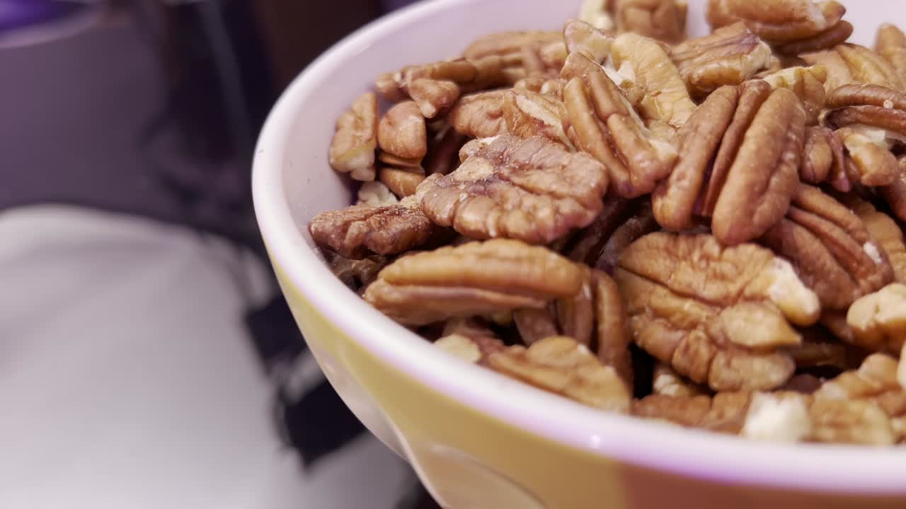 Ciotola di noci pecan su una superficie riflettente, con un primo piano delle noci.