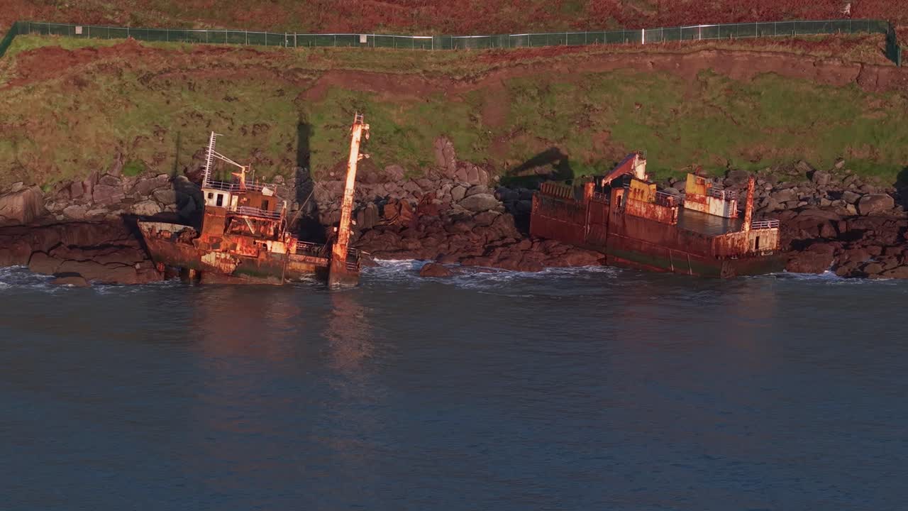 A fishing boat wreck rests on rocks at Ballycotton cliffs during golden hour in Ireland