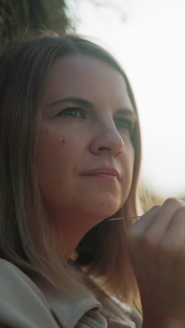 primer plano de una mujer en profundo pensamiento sosteniendo un hilo de heno, mirando a la distancia, la cálida luz dorada mejora el fondo borroso, creando un sereno y reflexivo