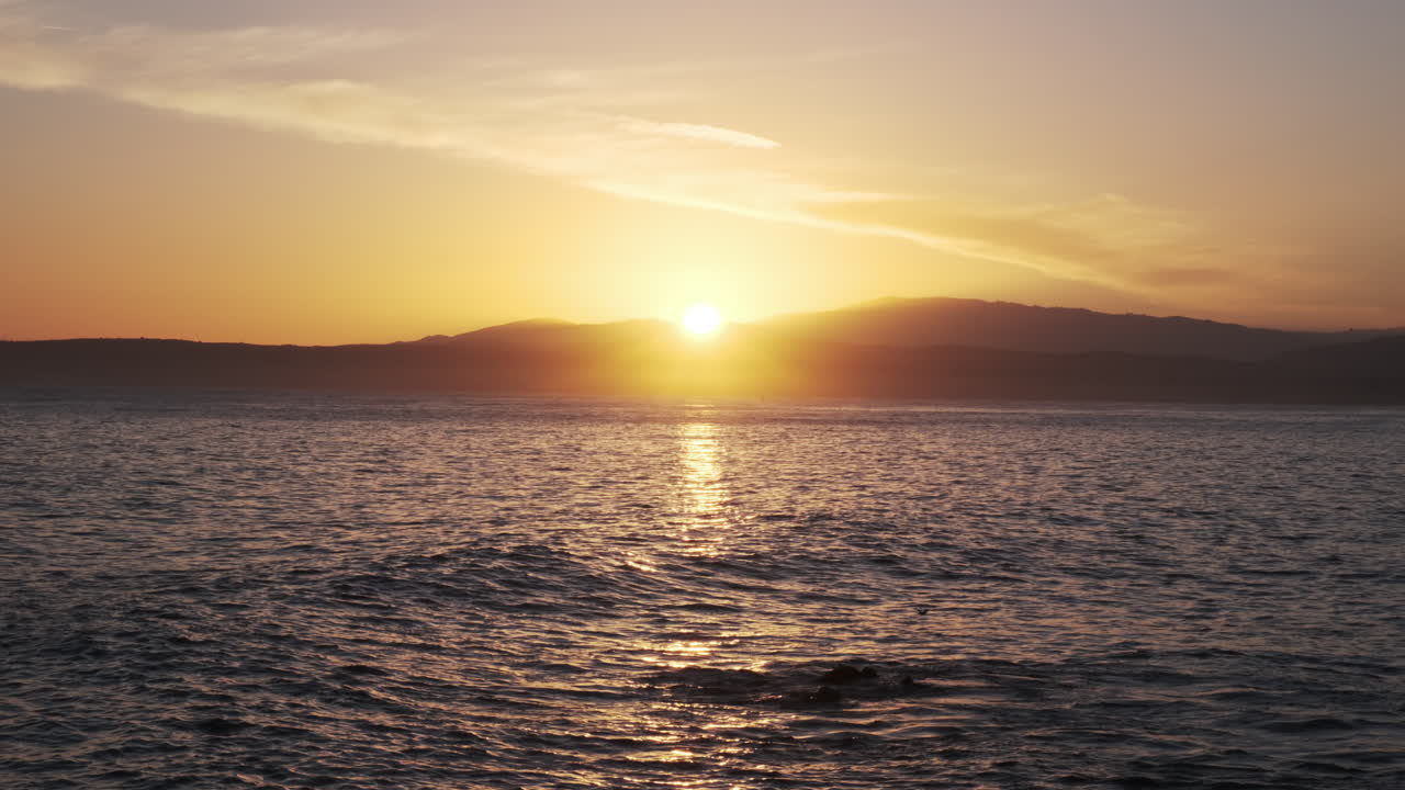 Brilliant sunset casts a radiant golden glow across the ocean, the sun dipping behind silhouetted mountains