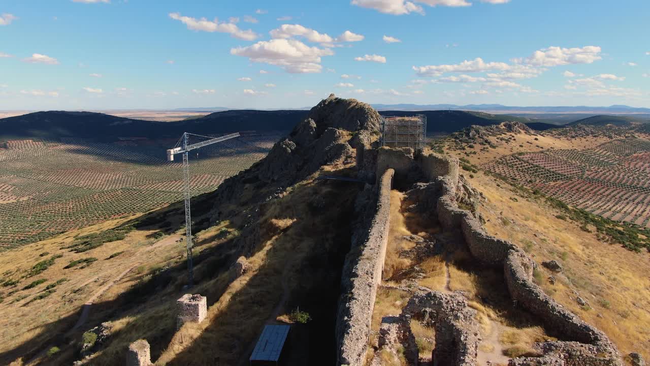 Un drone scende mentre la camera si inclina verso l'alto, mostrando la forma allungata simile a una nave del castello, la sua posizione sulla cima rocciosa e la torre principale in fase di restauro.