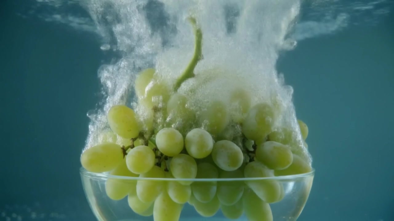 Uva verde che cade in una ciotola di vetro d'acqua