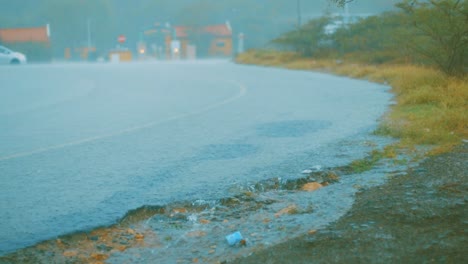 Slow-motion-shot-of-rain-streaming-down-a-quiet-road-in-Curacao-with-traffic-passing-in-the-distance