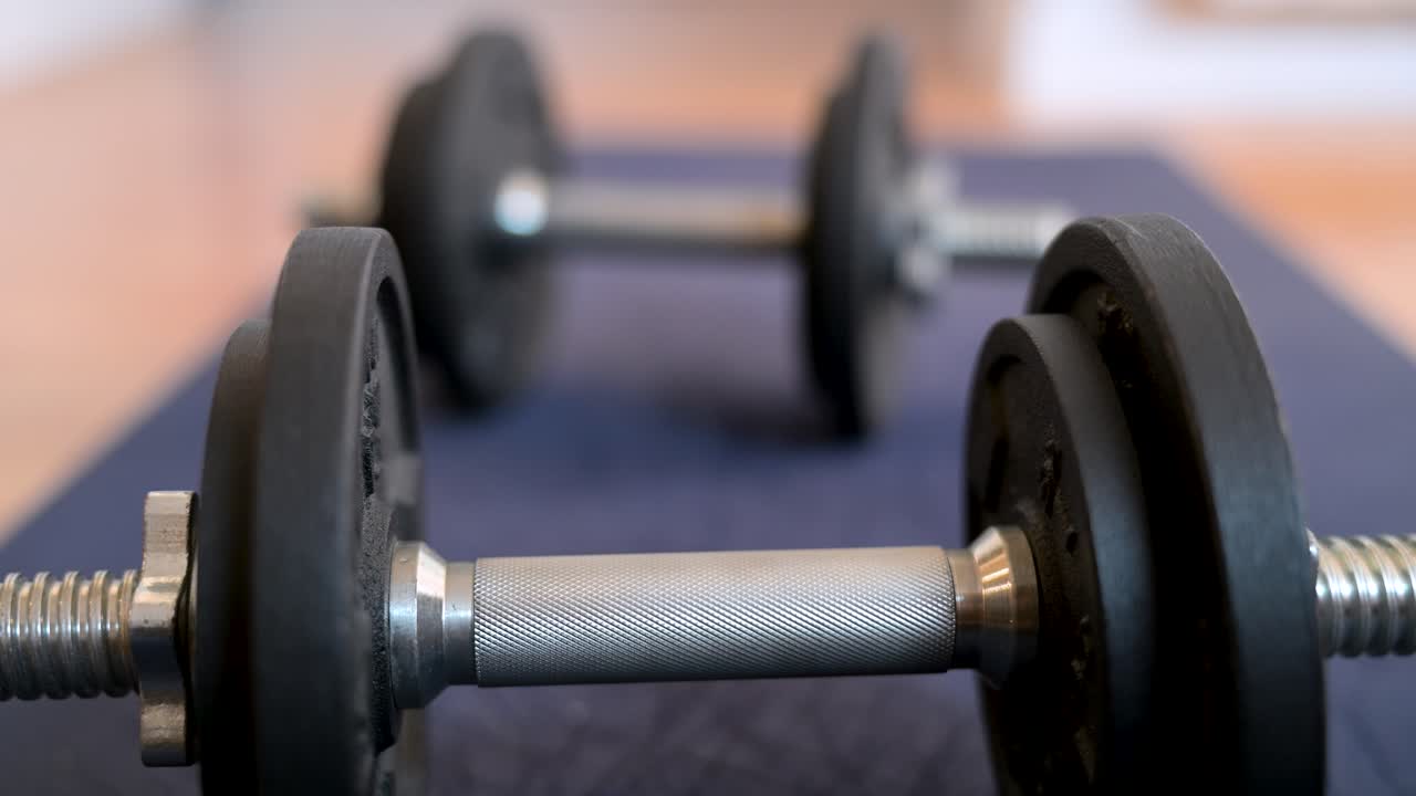 Extreme close-up on the textured, knurled grip of a dumbbell. The fitness equipment lies on a yoga mat, ready for a strength training or home workout session