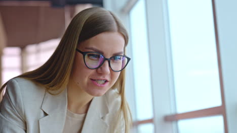 young woman in glasses and braces holding a phone in hand and looking at laptop. portrait of a smiling lady working in office. close up.