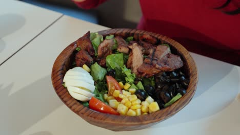 primer plano de la ensalada de cerdo a la parrilla de la mujer en un tazón de madera mientras comienza a comer