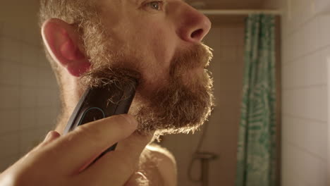 slow motion, a bearded man starts shaving off his long beard in a bathroom