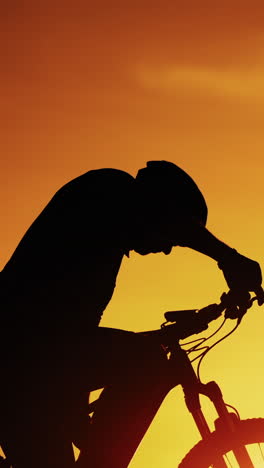 silhouette of a cyclist man is drinking water after intensive cycling training at sunset. biker drinks water from bottle and puts it into a bike on the natural golden sun setting background. vertical video