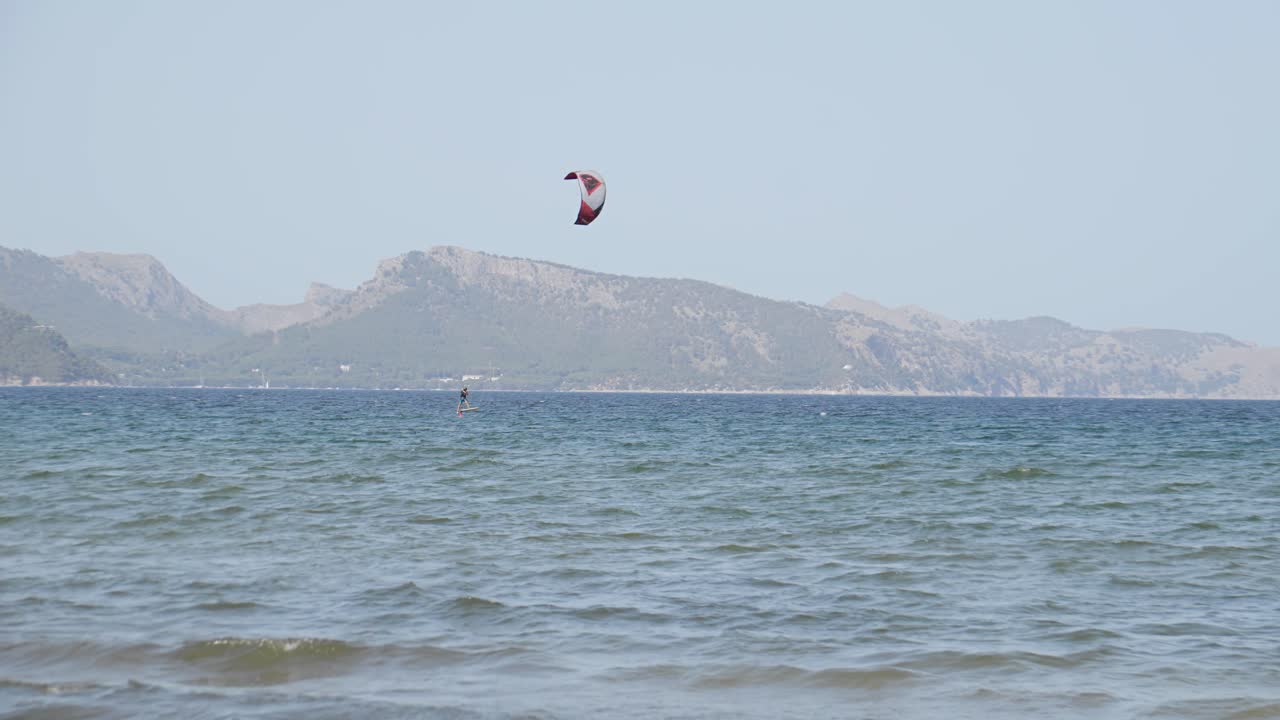 una persona practica kitesurf en agua azul cear en mallorca islas baleares rodeada de montaña