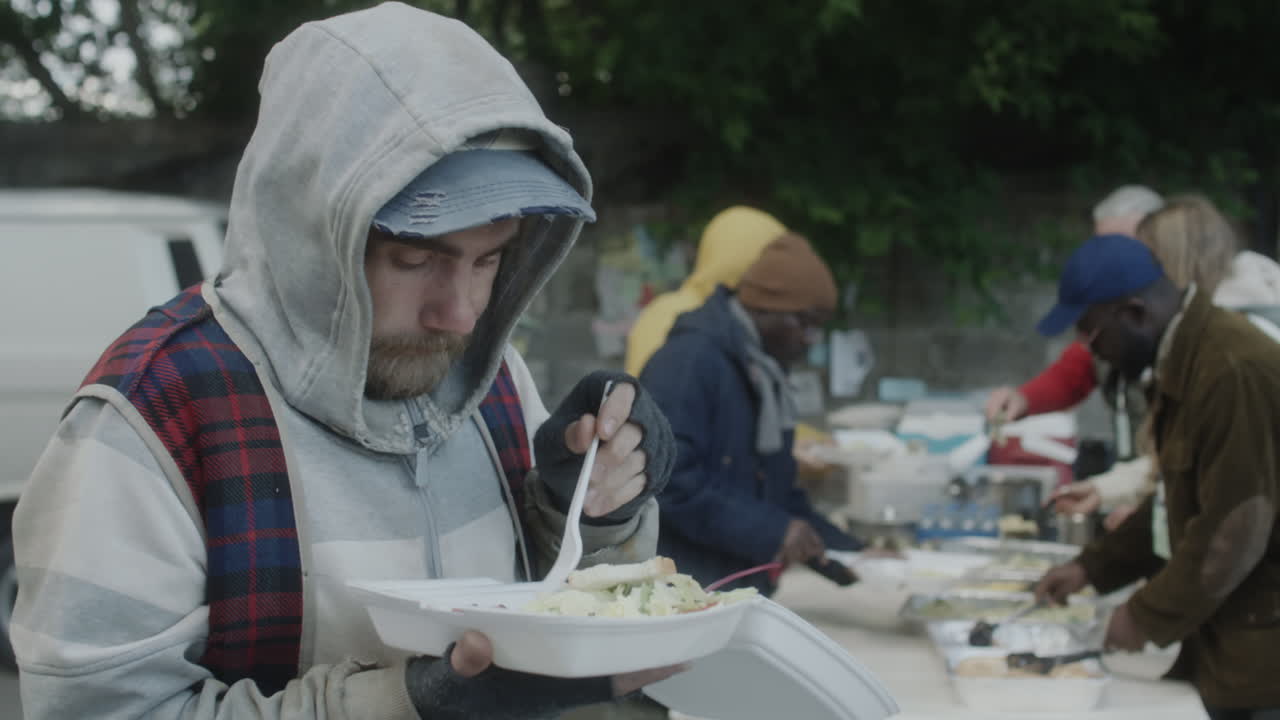 Obdachlose Menschen erhalten und verzehren Mahlzeiten bei einer karitativen Essensverteilung