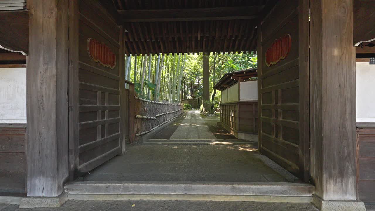 A traditional wooden gate at Myokoku-ji Temple opens to a pathway lined with a serene bamboo grove, inviting peaceful exploration of this historic Japanese site.