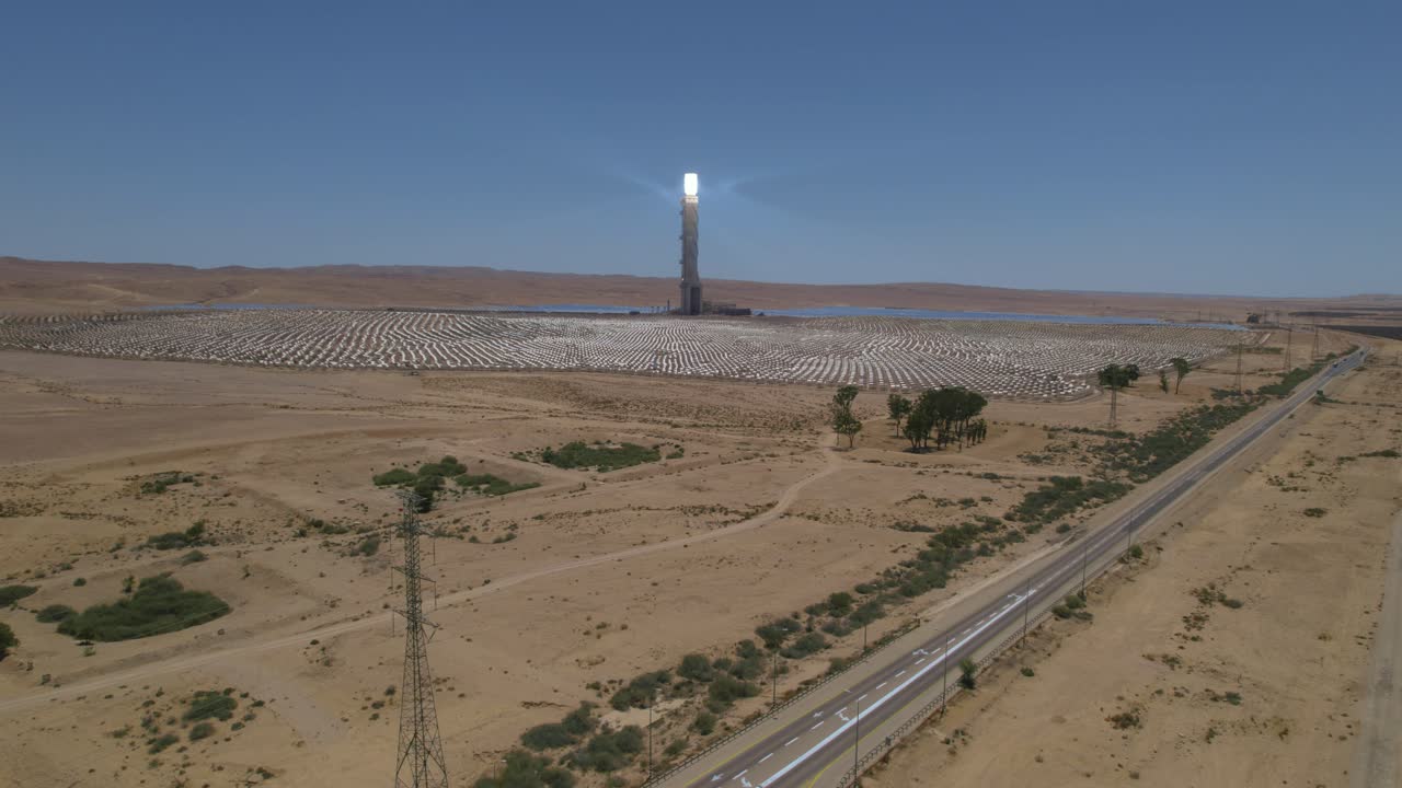 Ripresa aerea che si eleva di fronte a un impianto solare a concentrazione in un deserto desolato vicino a una strada.