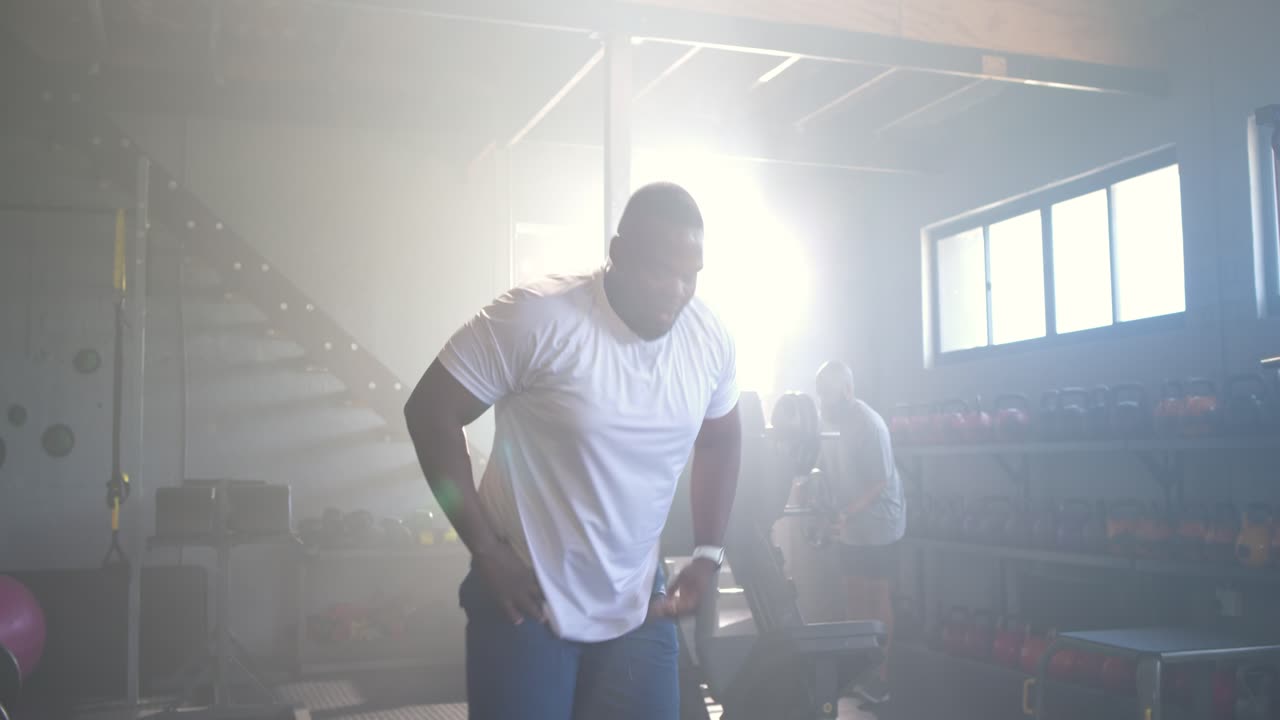 Afroamerikanske mænd træner i et fitnesscenter, fit mand griber fat i battle ropes, laver bølger og fanger vejret.