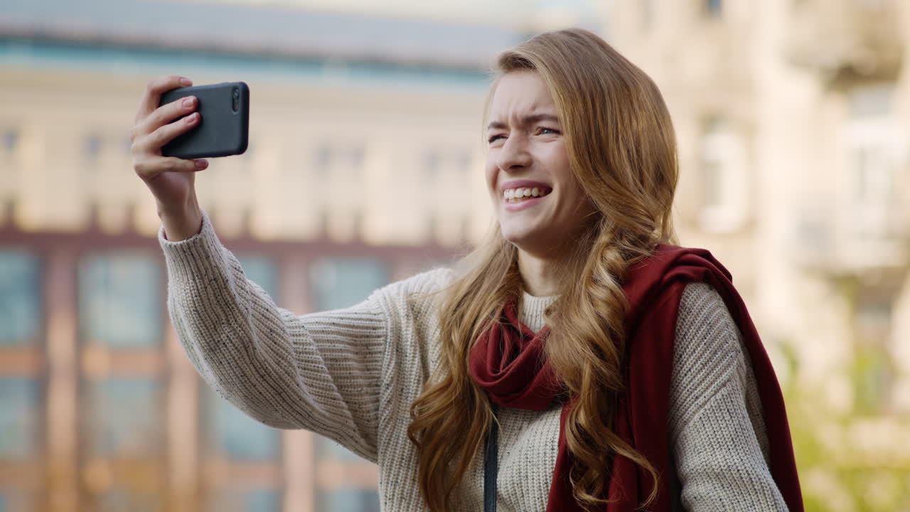 chica graciosa posando para la cámara del teléfono. mujer con muecas tomando selfies por teléfono al aire libre