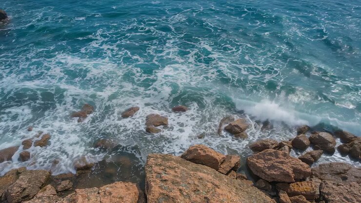 Onde turchesi spinte dalla risacca che si infrangono sul litorale roccioso, lambendo i massi