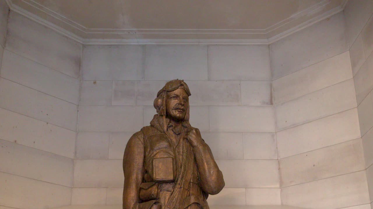 Un'inquadratura statica dal basso di una statua di aviatore in bronzo su una parete di pietra