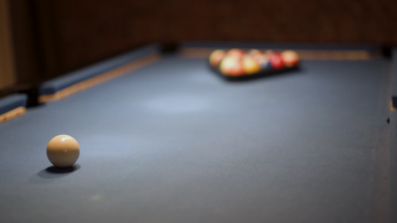 Individual arranges pool balls on billiard table, low ambient lighting, shallow depth of field