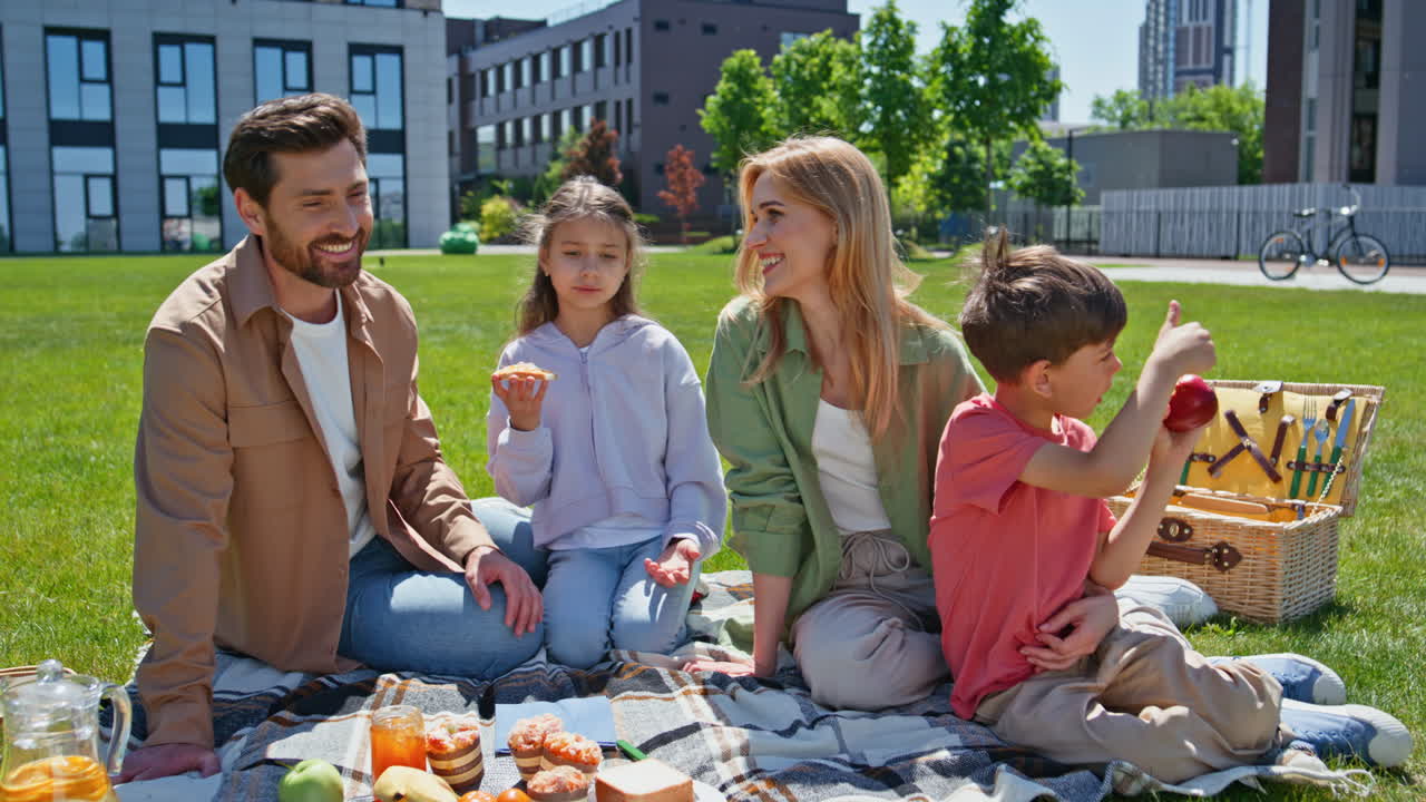 Parents kids enjoy picnic on green grass near apartment. Family children eating