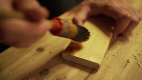 Close-up of applying a wood stain to a piece of wood using a paintbrush