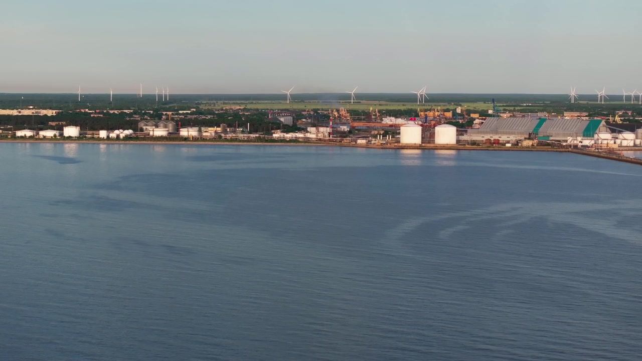 Ampio panorama aereo con drone che domina il porto industriale di Ventspils, Lettonia. Il filmato cattura terminal petroliferi, impianti di stoccaggio del petrolio, infrastrutture del porto merci, magazzini e turbine eoliche su