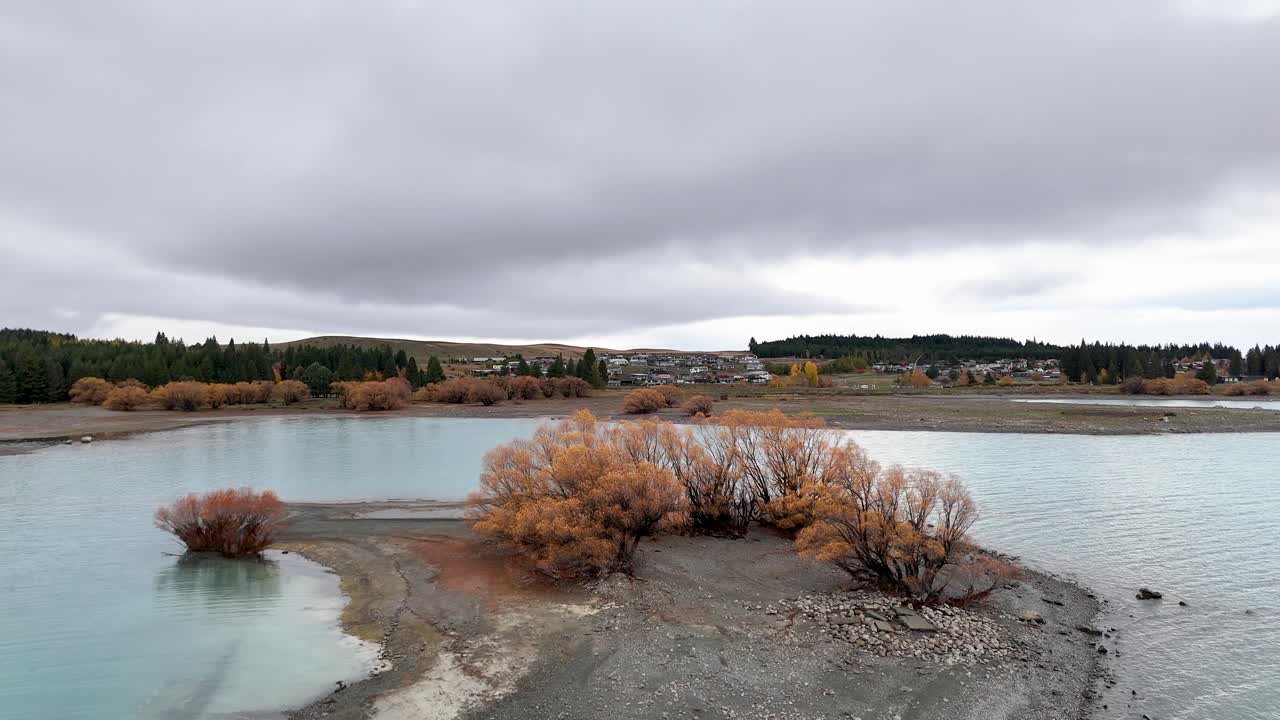 Aerial footage of Lake Tekapo captures tranquil autumn scenery with vibrant foliage and calm waters under overcast skies