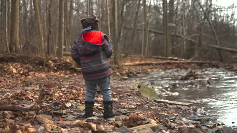 A-toddler-boy-throws-a-rock-into-a-river-on-a-cold,-autumn-day,-slow-motion