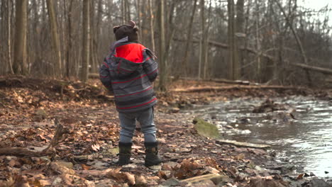 a toddler boy throws a rock into a river on a cold, autumn day, slow motion