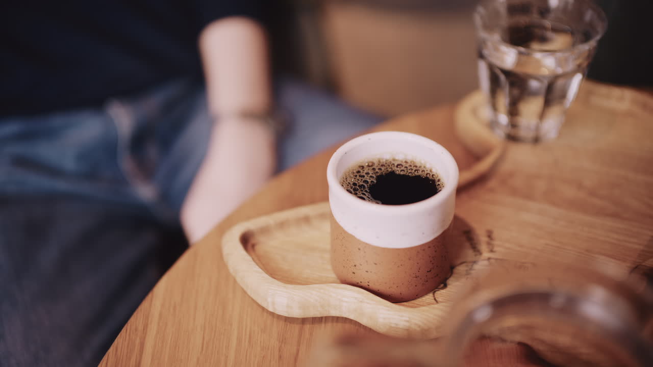 Primo piano di una piccola tazzina di ceramica piena di caffè espresso appena fatto, posizionata su un vassoio di legno su un tavolo da caffè