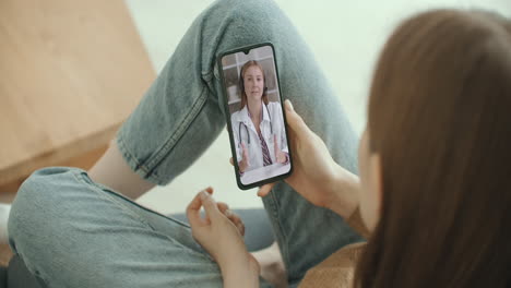 Female-medical-assistant-wears-white-coat-headset-video-calling-distant-patient-on-smartphone.-Doctor-talking-to-client-using-virtual-chat-telephone-app.-Telemedicine-remote-healthcare-services