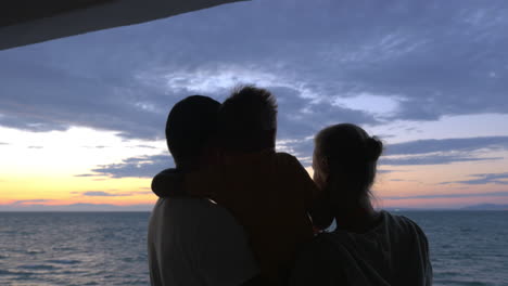 el hijo está abrazando a la madre y el padre contra el atardecer del mar