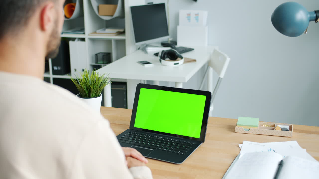 Person working on a laptop with green screen in an office