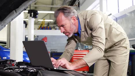 mechanic using laptop while servicing a car engine