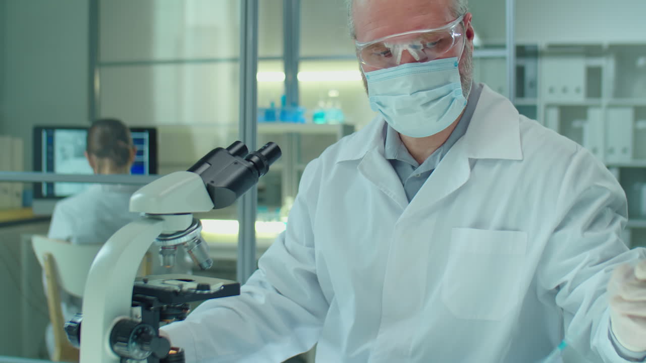 Masked Senior Scientist Examining Specimen under Microscope