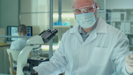 masked senior scientist examining specimen under microscope