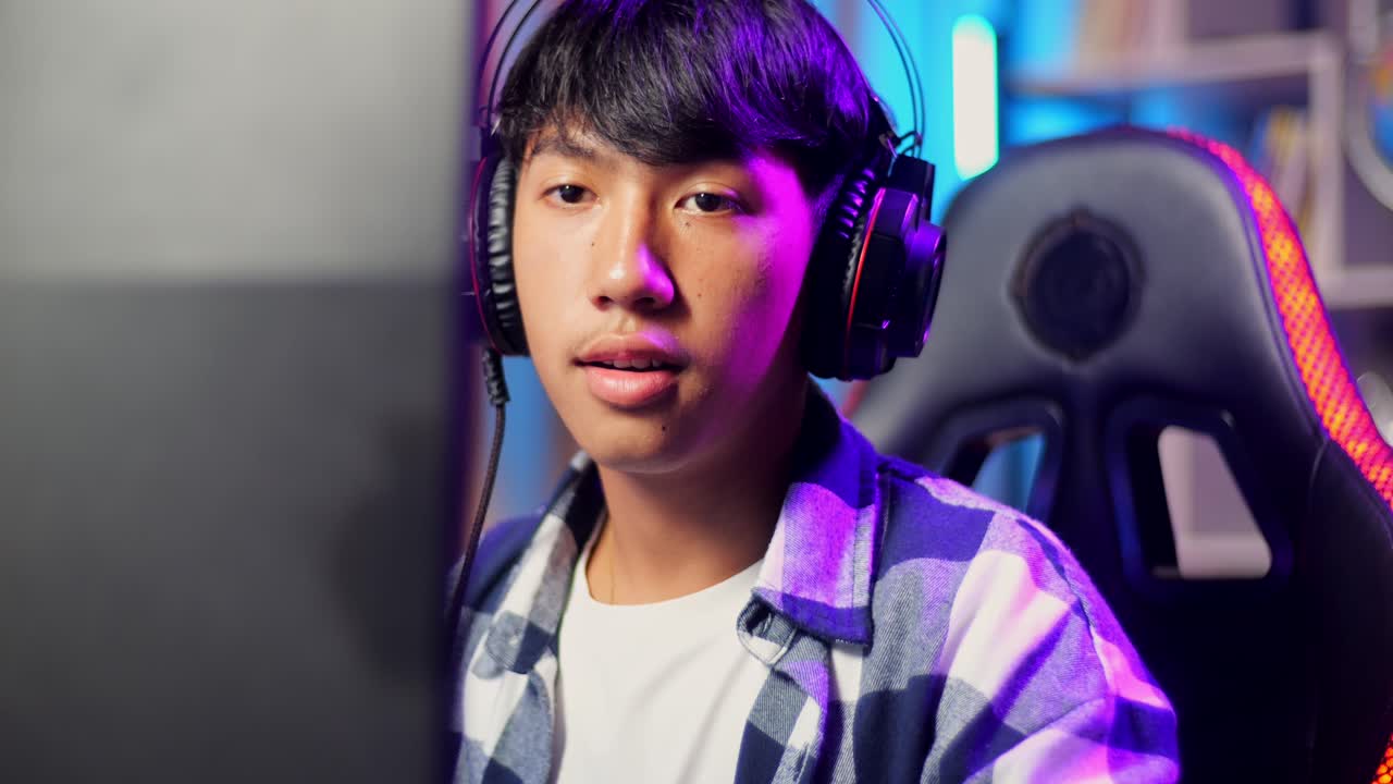 컴퓨터에서 비디오 게임을 하는 동안 팔을 고 카메라에 미소 짓는 아시아 십대 소년 게이머의 클로즈업