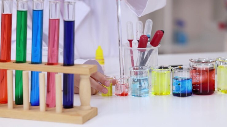 En videnskabsmand i en hvid laboratoriekittel bruger en pipette med farverige kemikalier i bægerglas.