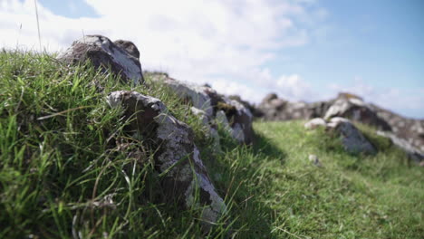 closeup of rocks covered in grass with blue sky and clouds in the background.