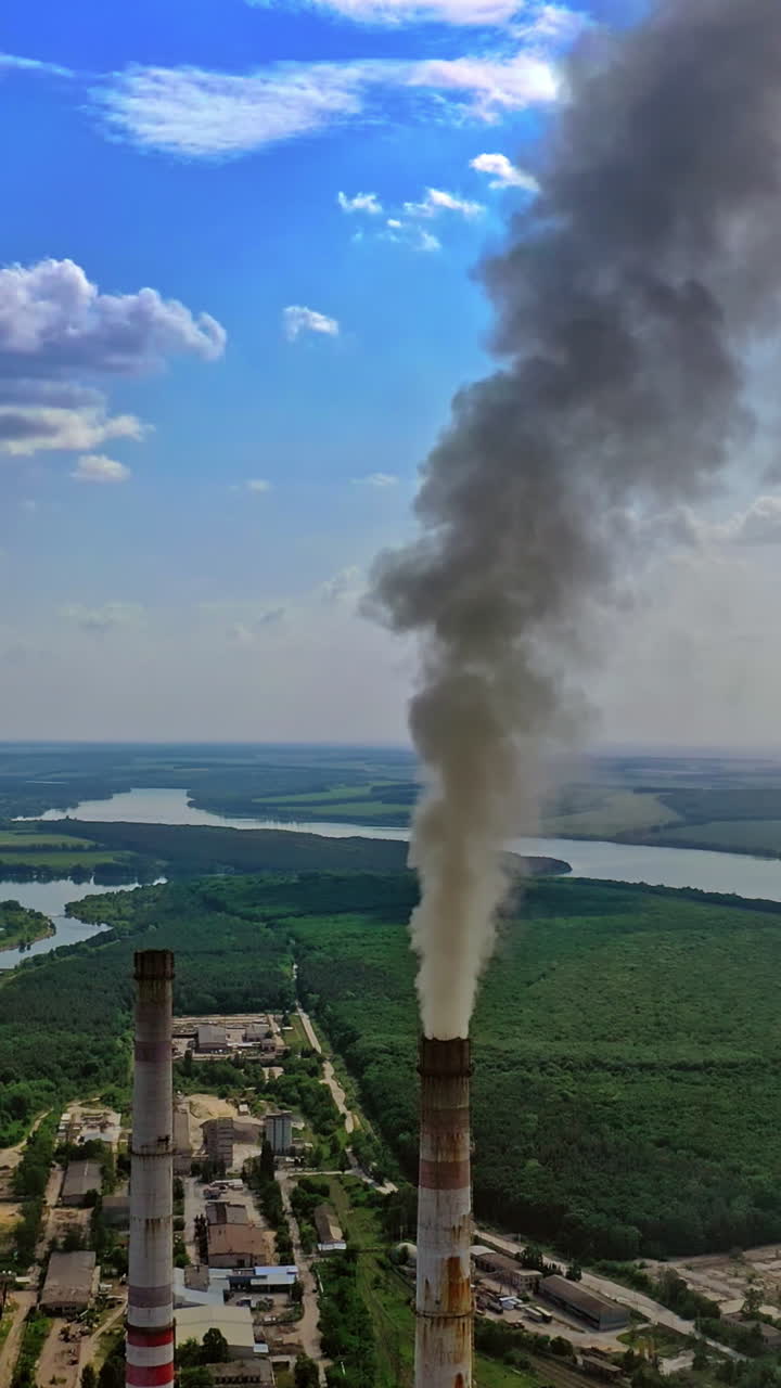 Dirty smoke from industrial pipe. Manufacturing with pipes on nature background with green fields and river. Pollution of environment. Vertical video