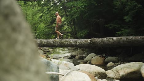 bald guy balances over river on fallen tree bridge super slomo