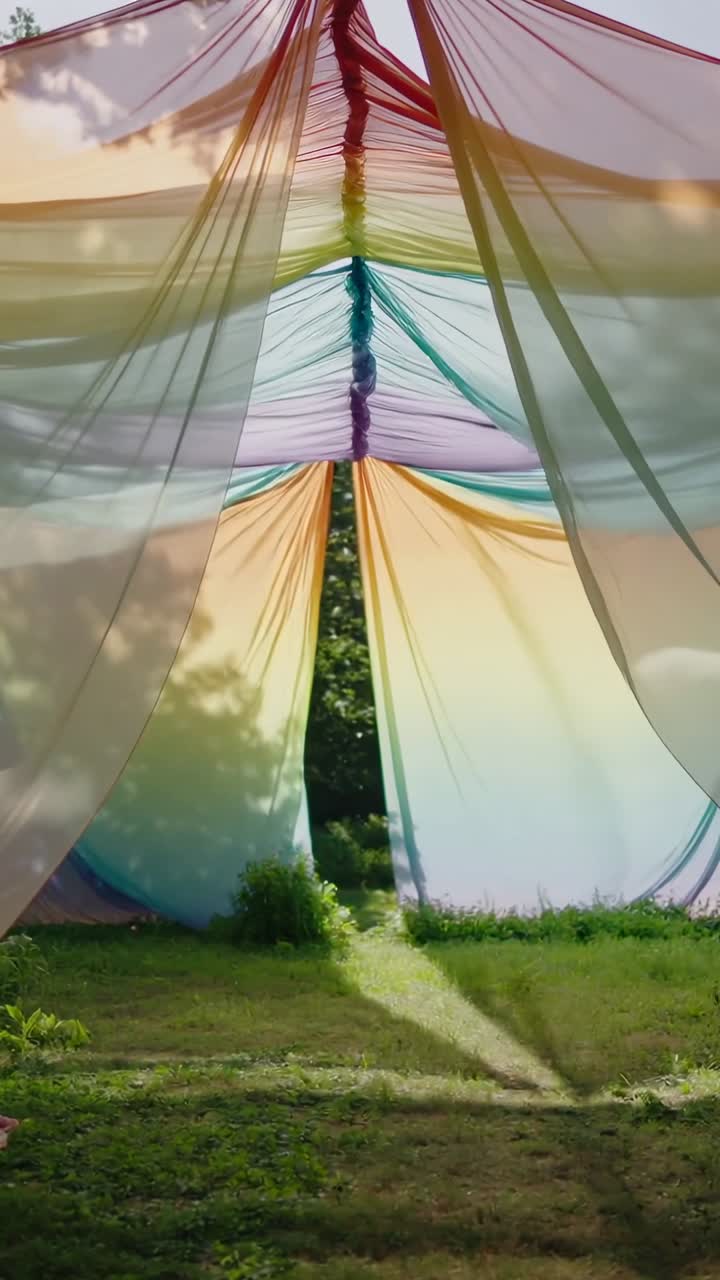 Video verticale: Tenda arcobaleno ondeggiante che si muove in giardino, rivelando una cucitura aperta e una chiazza di sole.