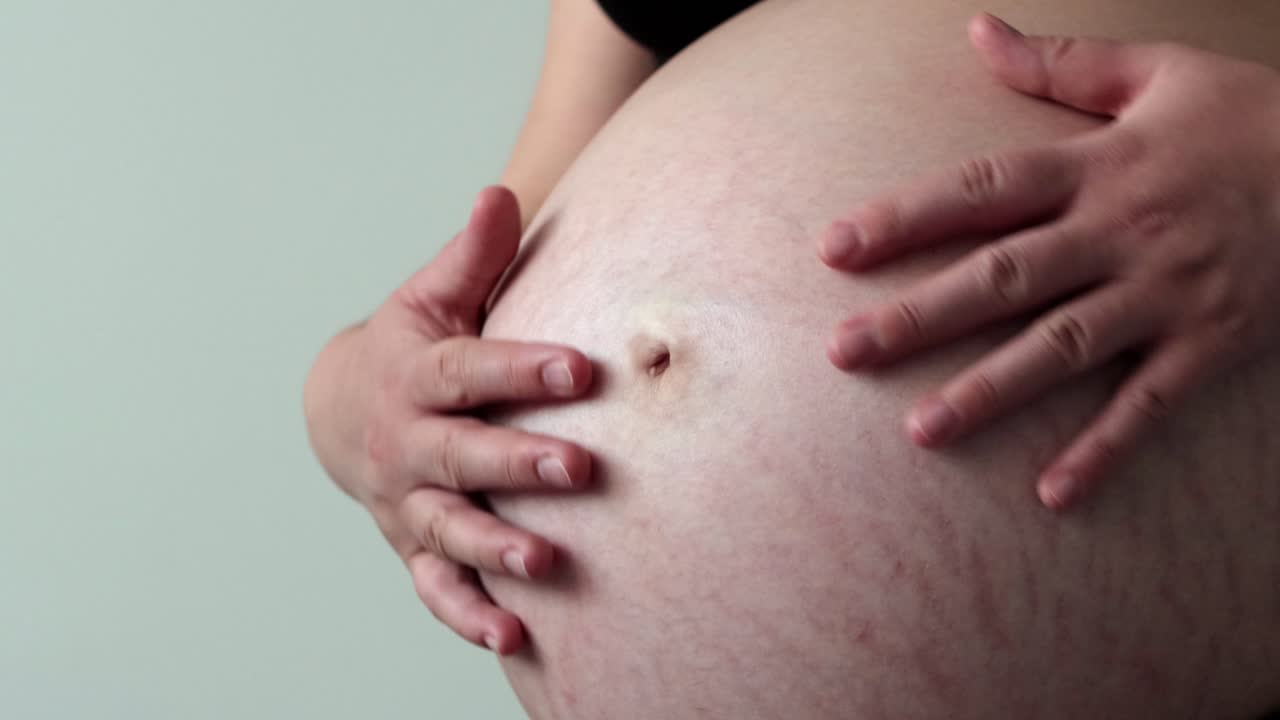 Pregnant woman in third trimester gently rubs belly with her hands. Close up