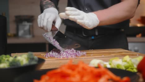 cebolla recién picada cortada en una tabla de madera por un chef profesional con un elegante pantalones negro con tatuajes y guantes blancos